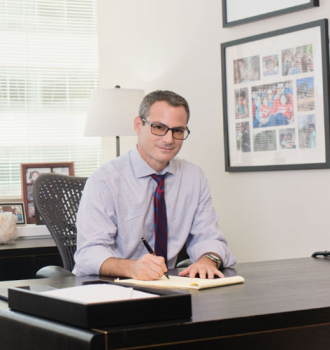 Attorney Howard "Howie" A. Rosen sitting at his desk with family portraits behind him
