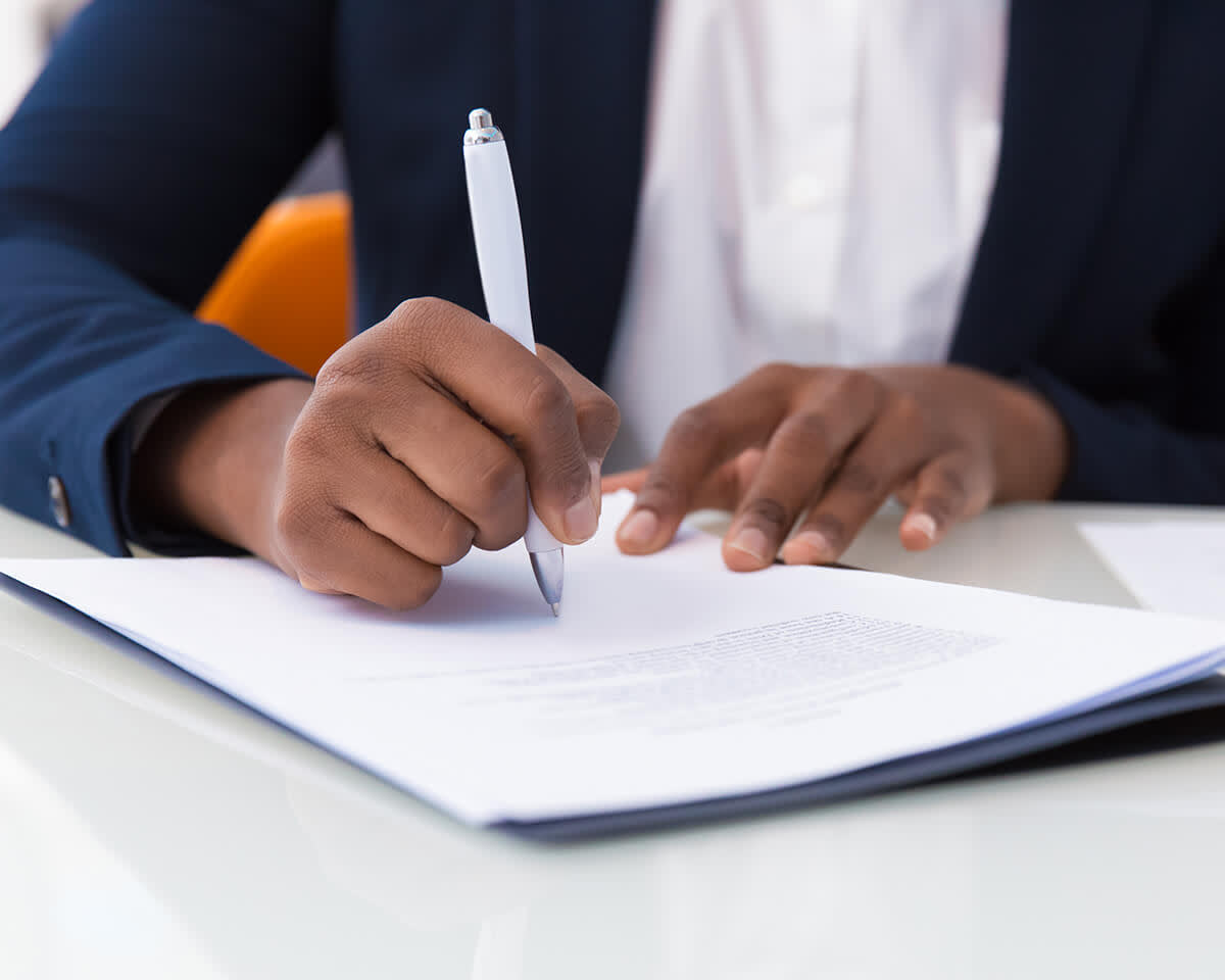 Businesswoman signing contract. African American business woman sitting at table in office, holding pen and writing in document.