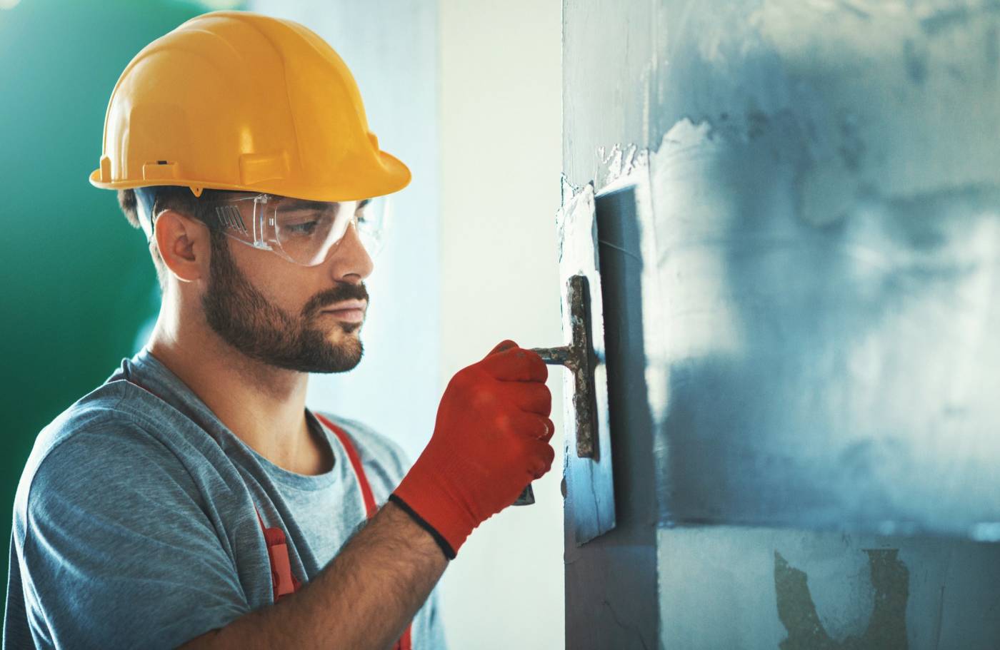 Male construction worker with hard hat smoothing the walls with a scraper