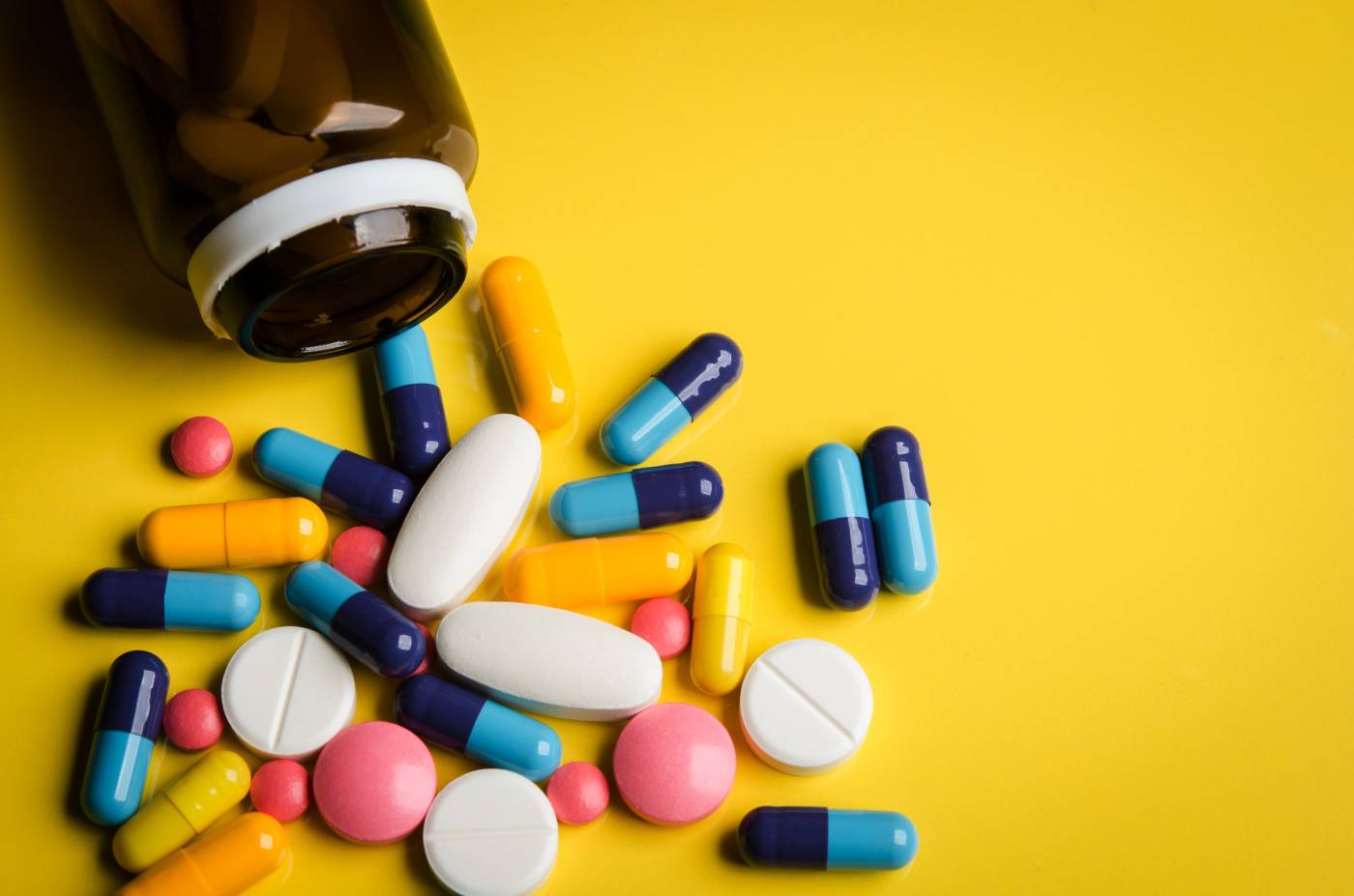 Bottle of brightly colored pills on a bright yellow surface