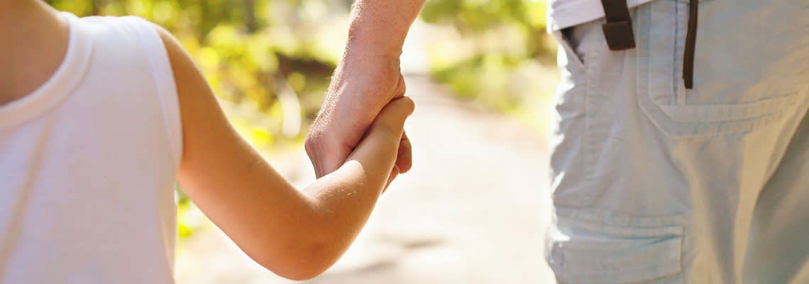 A child holding a parent's hand on a pathway