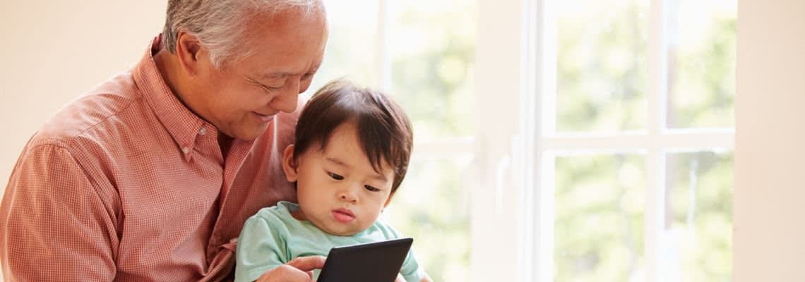 An old man holding a baby, showing it a tablet